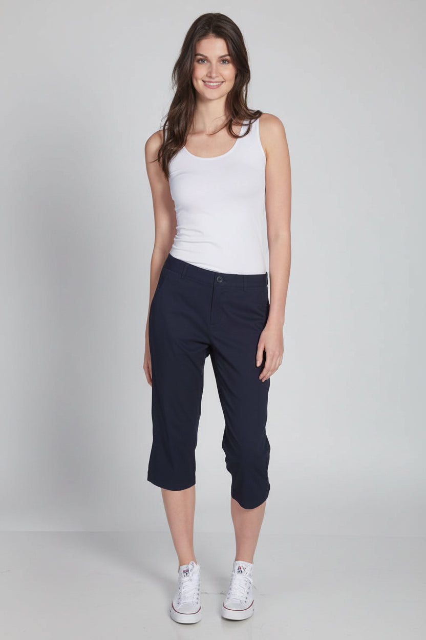 Woman wearing a white tank top and navy capri pants on a white background