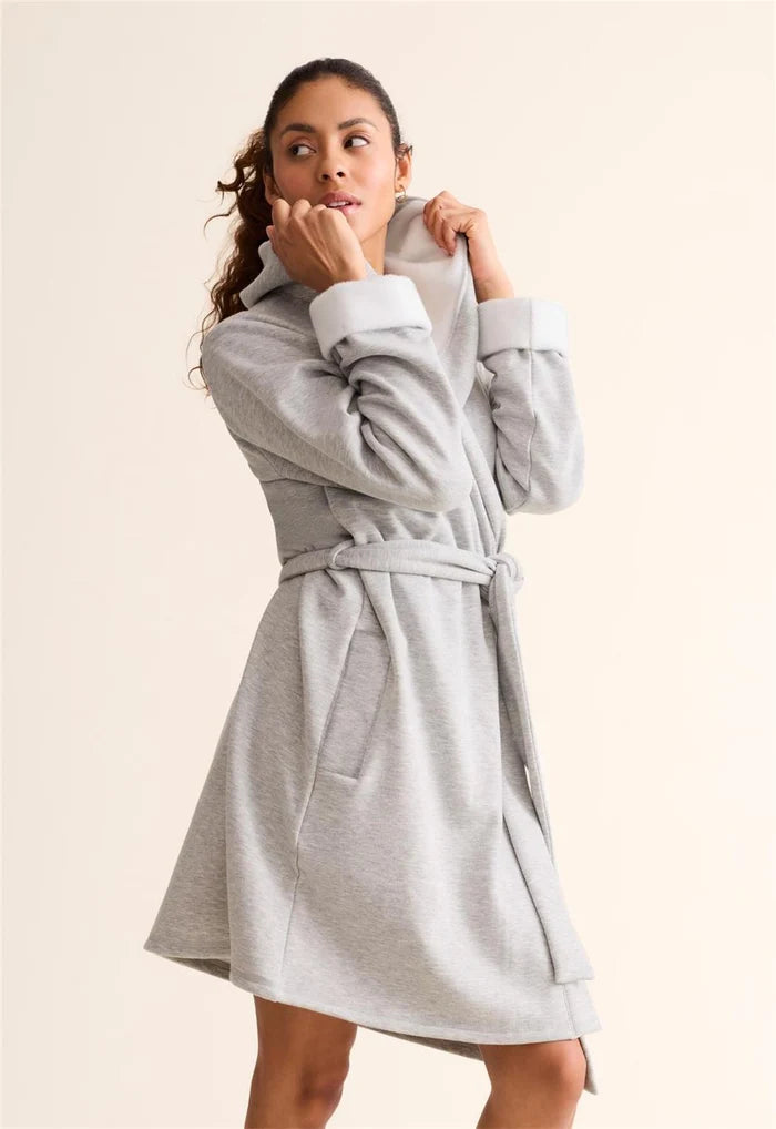A woman wearing a light gray heathered hooded robe with a matching belt, standing against a plain beige studio background.