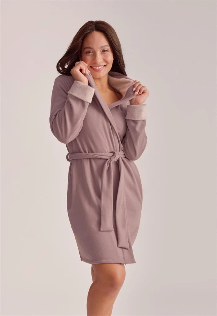 A woman modeling a dusty mauve bathrobe with a tie waist and ribbed cuffs, photographed against a solid light gray studio background.