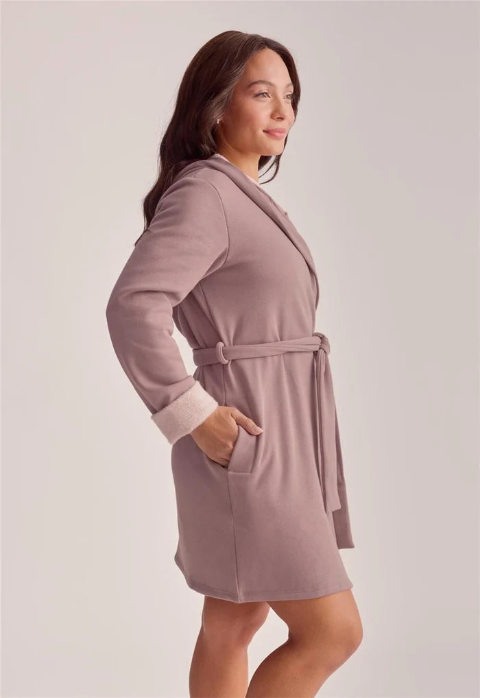 A woman wearing a dusty mauve bathrobe with a matching tie belt, shown from a side profile against a light gray studio background.