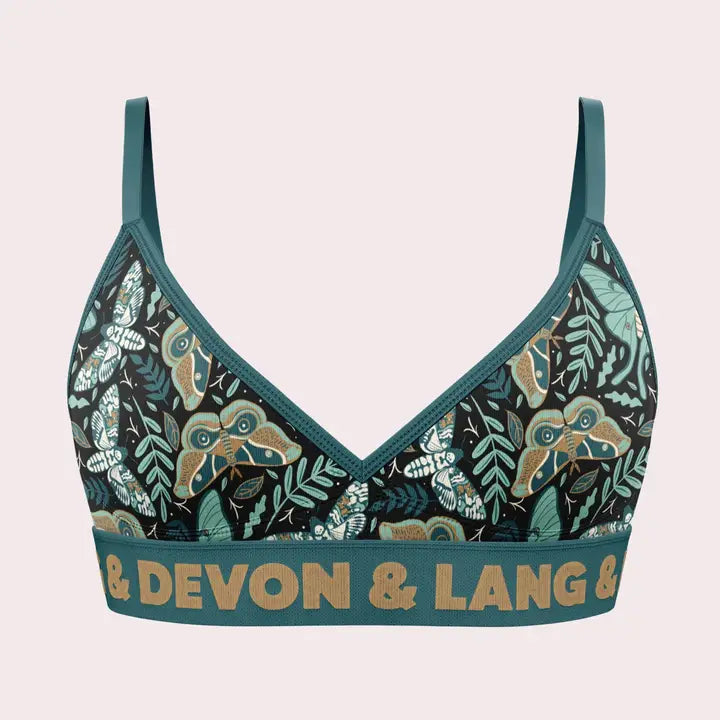 A women's bralette by Devon & Lang featuring a dark teal and black tropical leaf pattern with gold lettering on the underband, displayed against a light pink background.