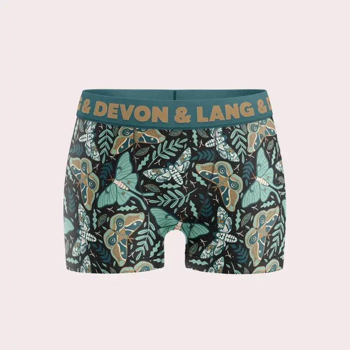 Men's boxer briefs by Devon & Lang featuring a dark green and black background with a detailed pattern of green, beige, and blue moths and leaves. The waistband is a solid dark green with the brand name printed in gold.