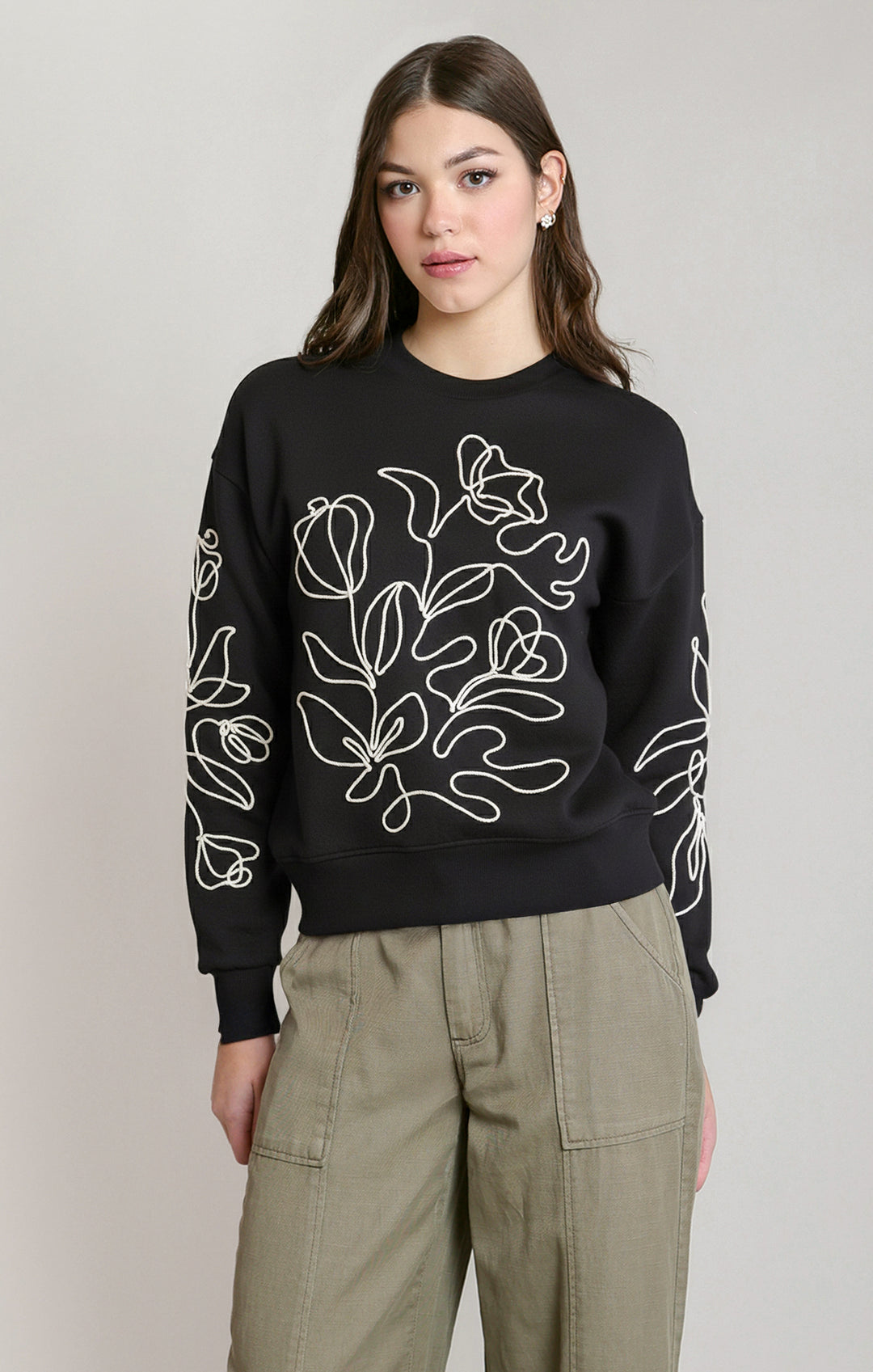 Person wearing a black sweater with white floral patterns on a plain background