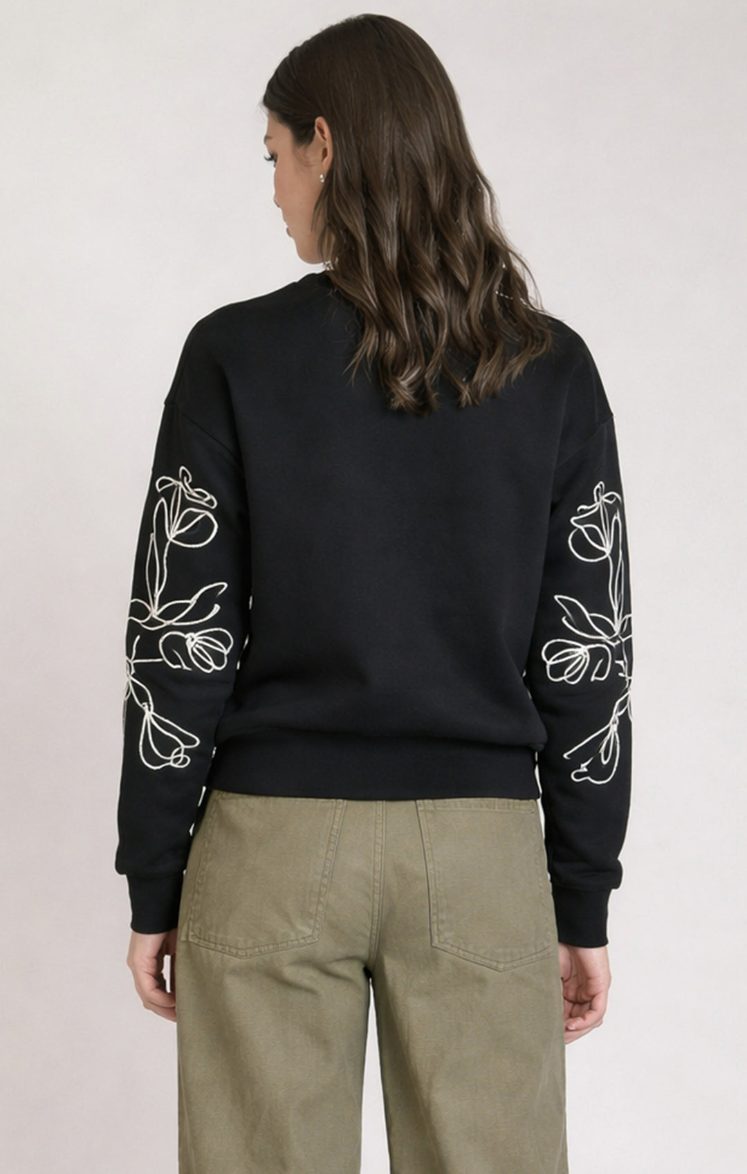 Person wearing a black sweatshirt with white floral patterns on sleeves against a plain background