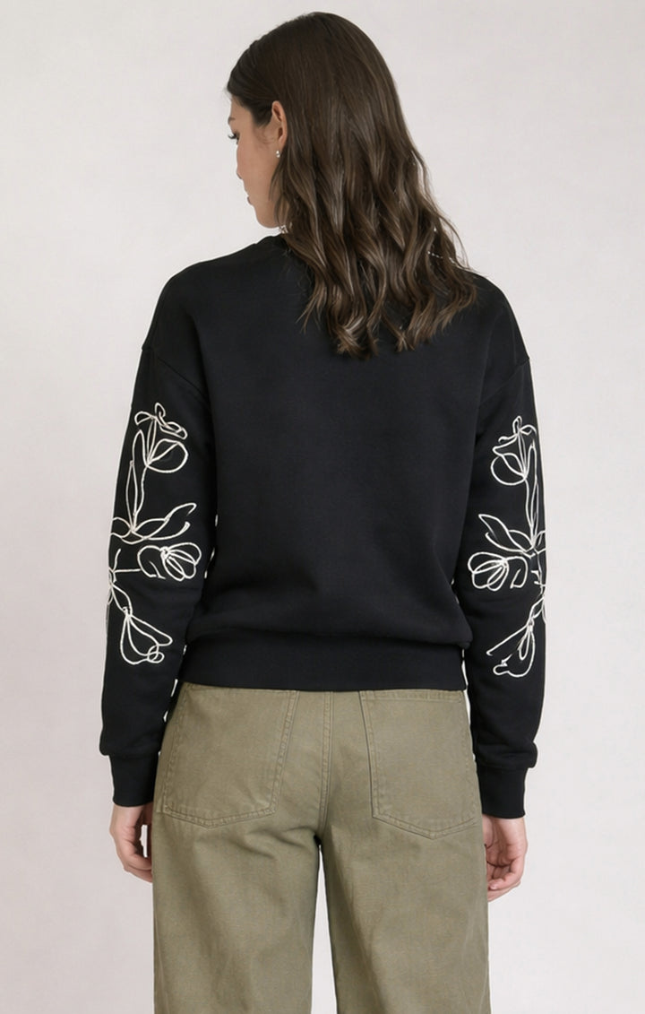 Person wearing a black sweatshirt with white floral patterns on sleeves against a plain background