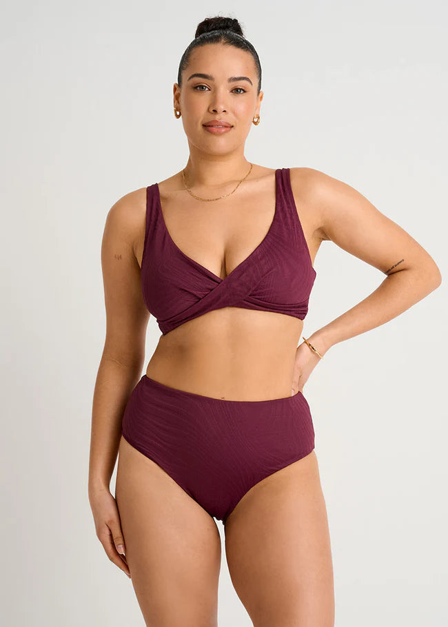 Woman wearing a maroon bikini set on a plain background