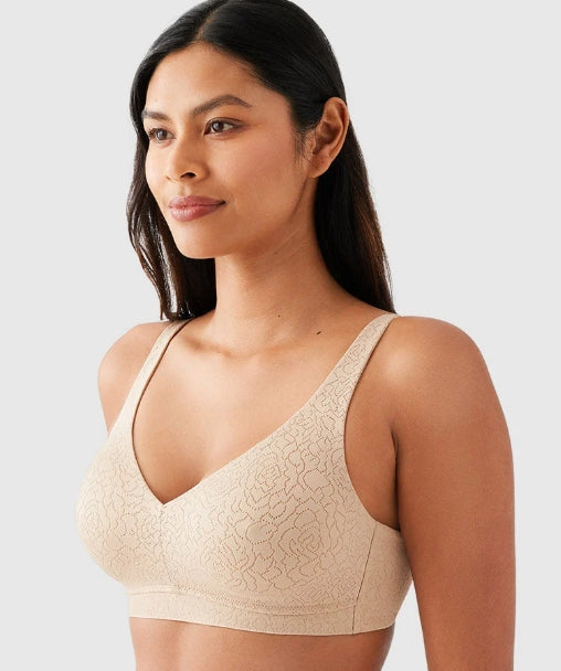 A woman wearing a beige floral lace bralette, shown from the chest up against a light gray studio background.