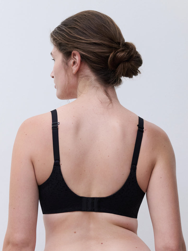 Rear view of a woman wearing a black underwire bra with adjustable shoulder straps and a center back strap, shown against a light gray studio background.