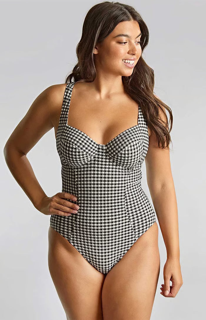 A woman modeling a one-piece swimsuit with a black and white houndstooth pattern against a light gray studio background.