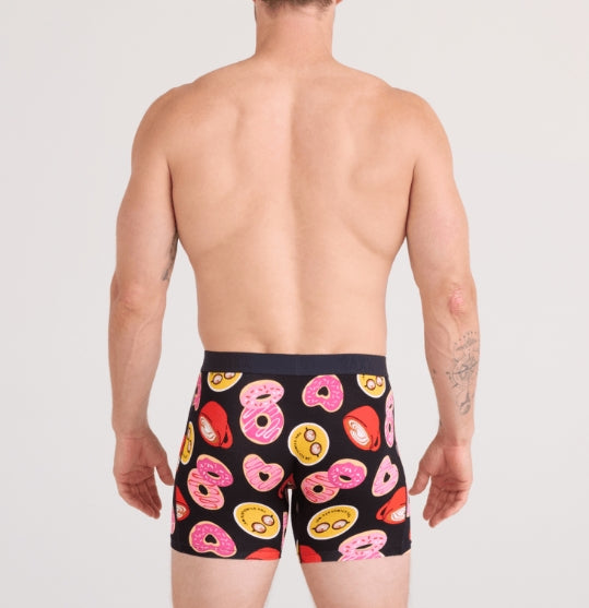 Person wearing black swim shorts with colorful donut pattern on a plain background