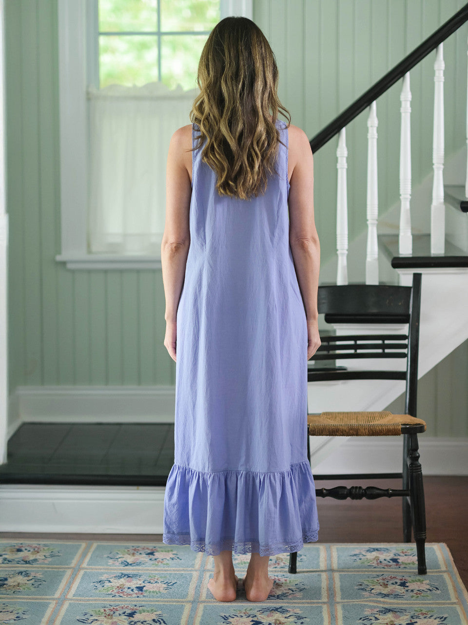 Woman in a long purple dress standing in a room with a staircase and window.