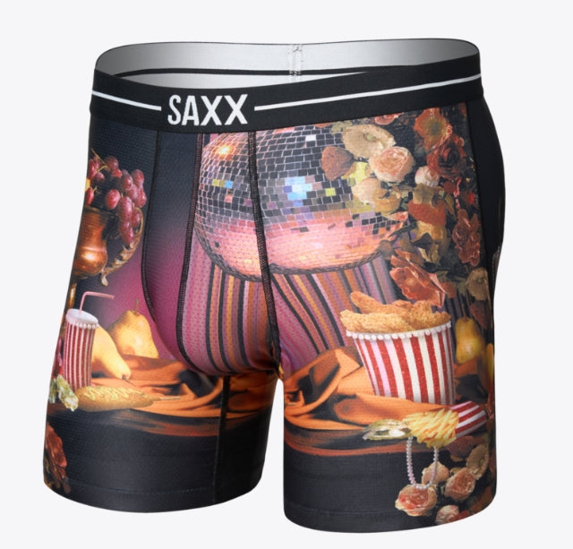 Boxer briefs featuring a dark graphic print with a disco ball, flowers, popcorn, and a drink, with the brand name 'SAXX' printed on the waistband.