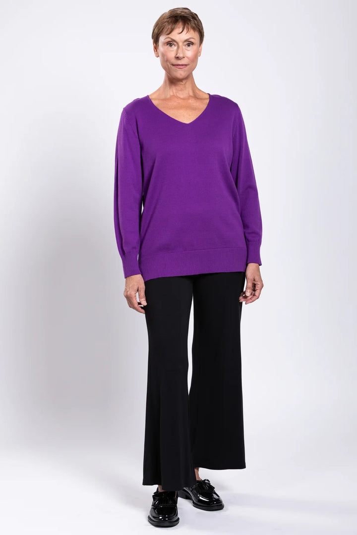 Woman wearing a purple long-sleeve top and black pants on a white background