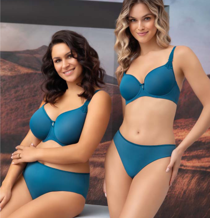 Two women modeling matching teal blue bra and panty lingerie sets against a scenic desert backdrop. The left model has dark wavy hair and wears a V-neck bra with a front zipper and matching high-waisted briefs.