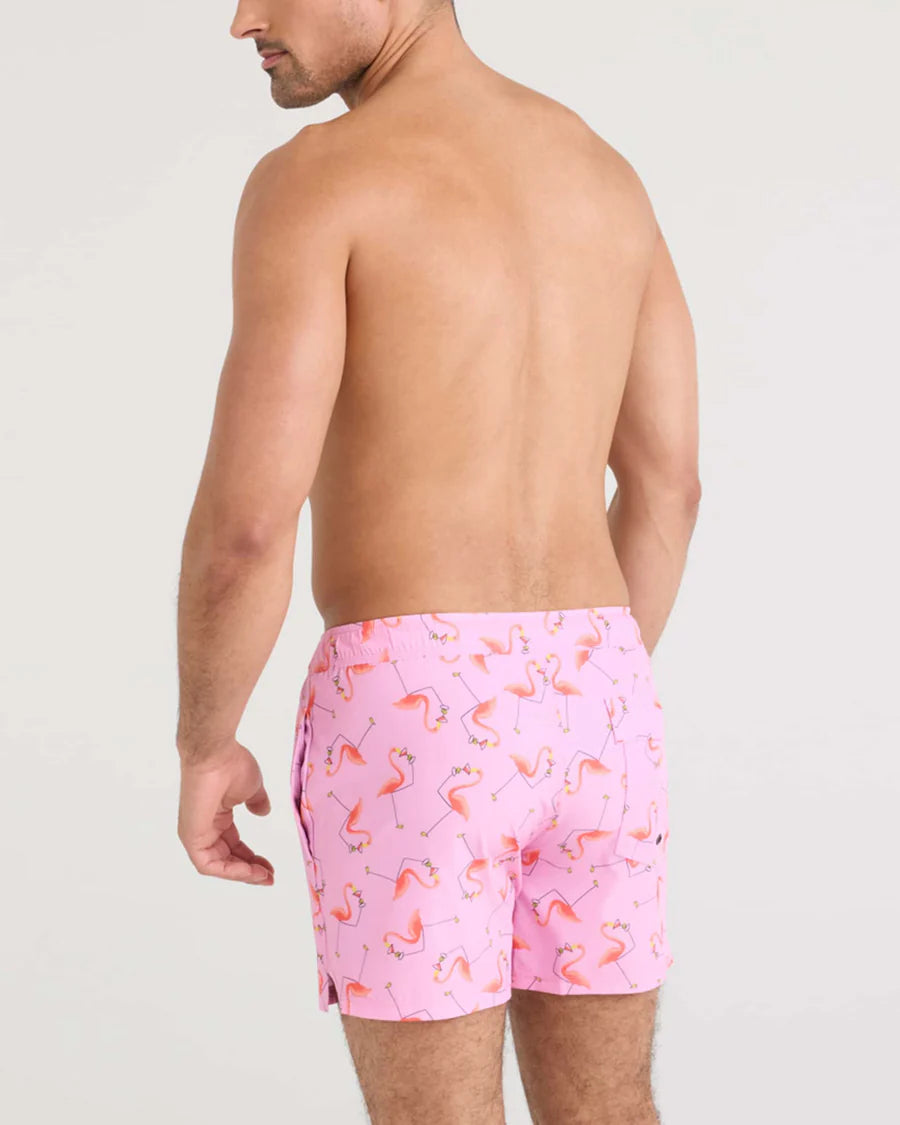 Man wearing pink flamingo patterned swim shorts on a plain background