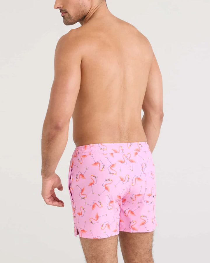 Man wearing pink flamingo patterned swim shorts on a plain background