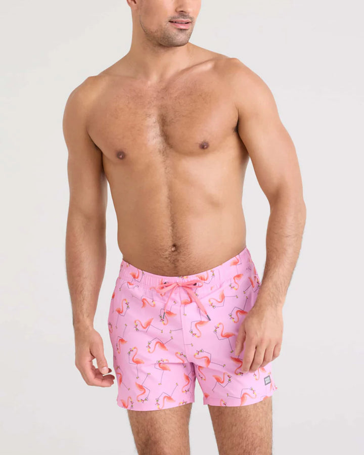 Man wearing pink flamingo patterned swim shorts on a plain background